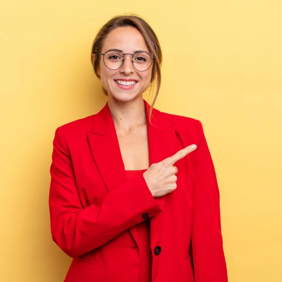 Moça loira de óculos e roupa social vermelha, sorrindo e apontando para o lado